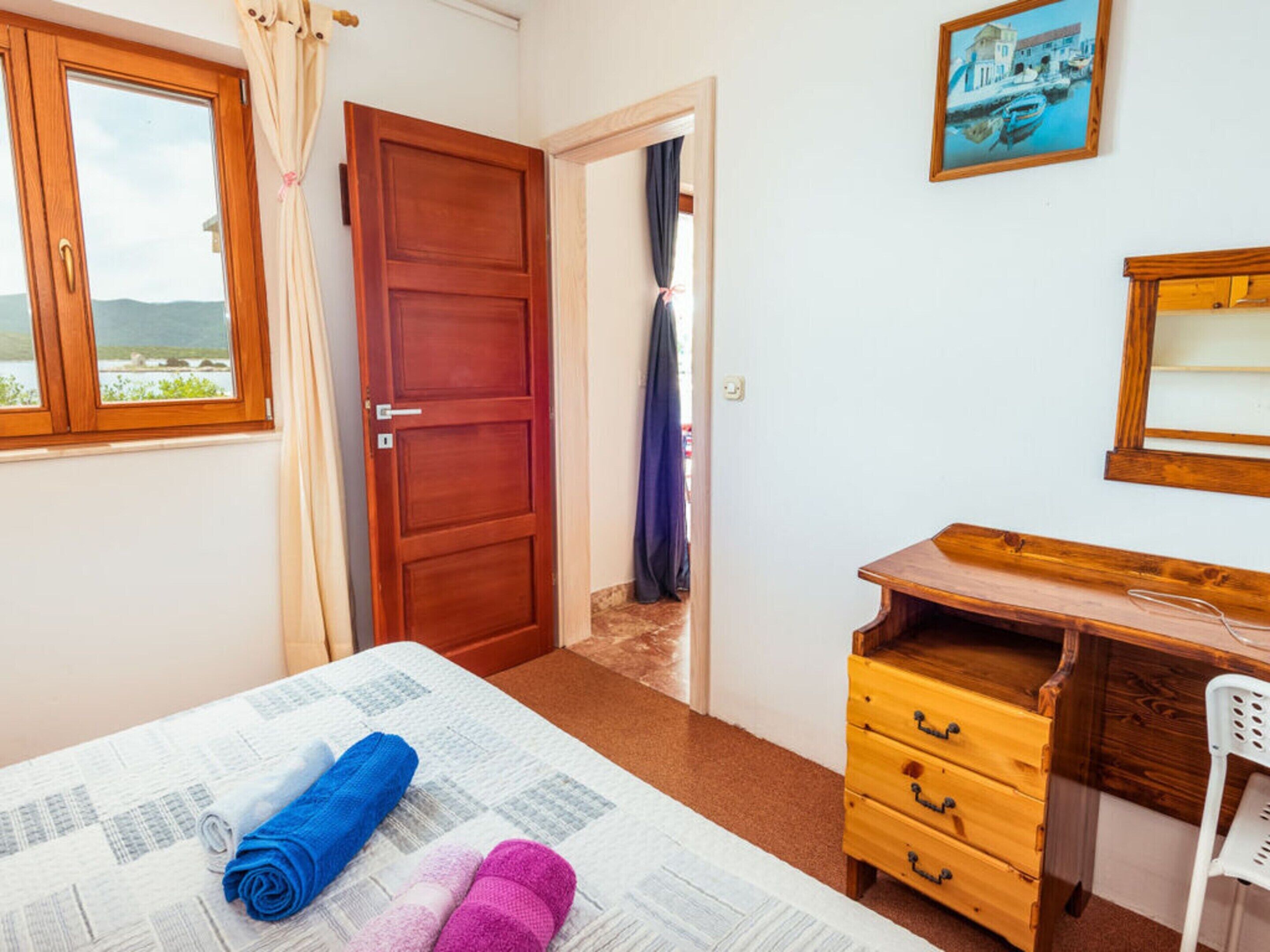 Une chambre à coucher avec un lit, une commode en bois, un bureau et une fenêtre donnant sur la mer.