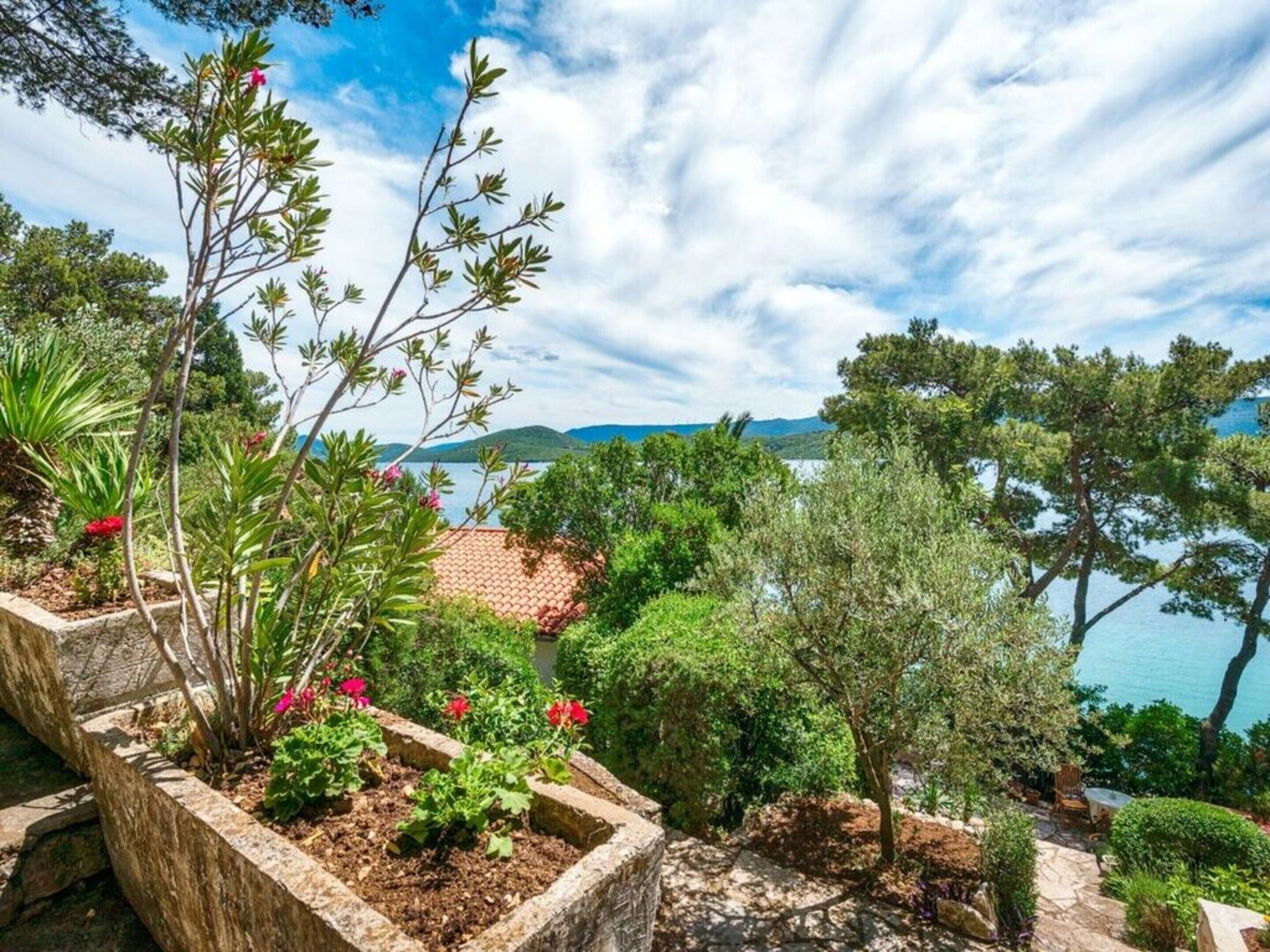 A garden with stone planters, a variety of plants, and a view of a body of water and hills in the distance.