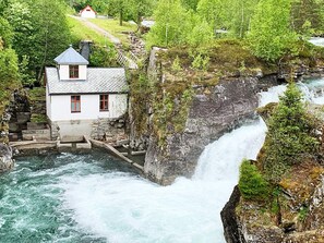 A white building with a red window and a grey roof near a waterfall. - 8 Person Holiday Home in Valldal (Fjord)