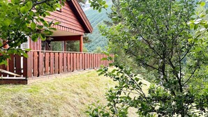 A wooden cabin with a balcony overlooking a grassy hillside and a forested mountain backdrop. - 8 Person Holiday Home in Valldal (Fjord)