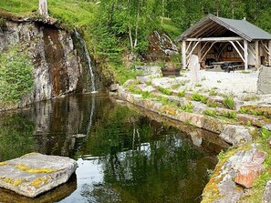 A rustic wooden cabin with a stone pathway leading to it, a small waterfall, and a calm pond. - 8 Person Holiday Home in Valldal (Fjord)