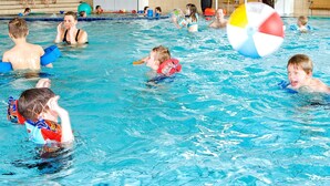 Uma piscina interior com várias pistas de natação, uma cadeira de salva-vidas e uma grande boia de praia insuflável.