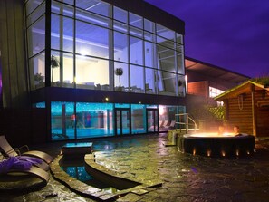 Un bâtiment moderne doté d’une façade en verre, d’une piscine et d’un espace équipé d’un jacuzzi.
