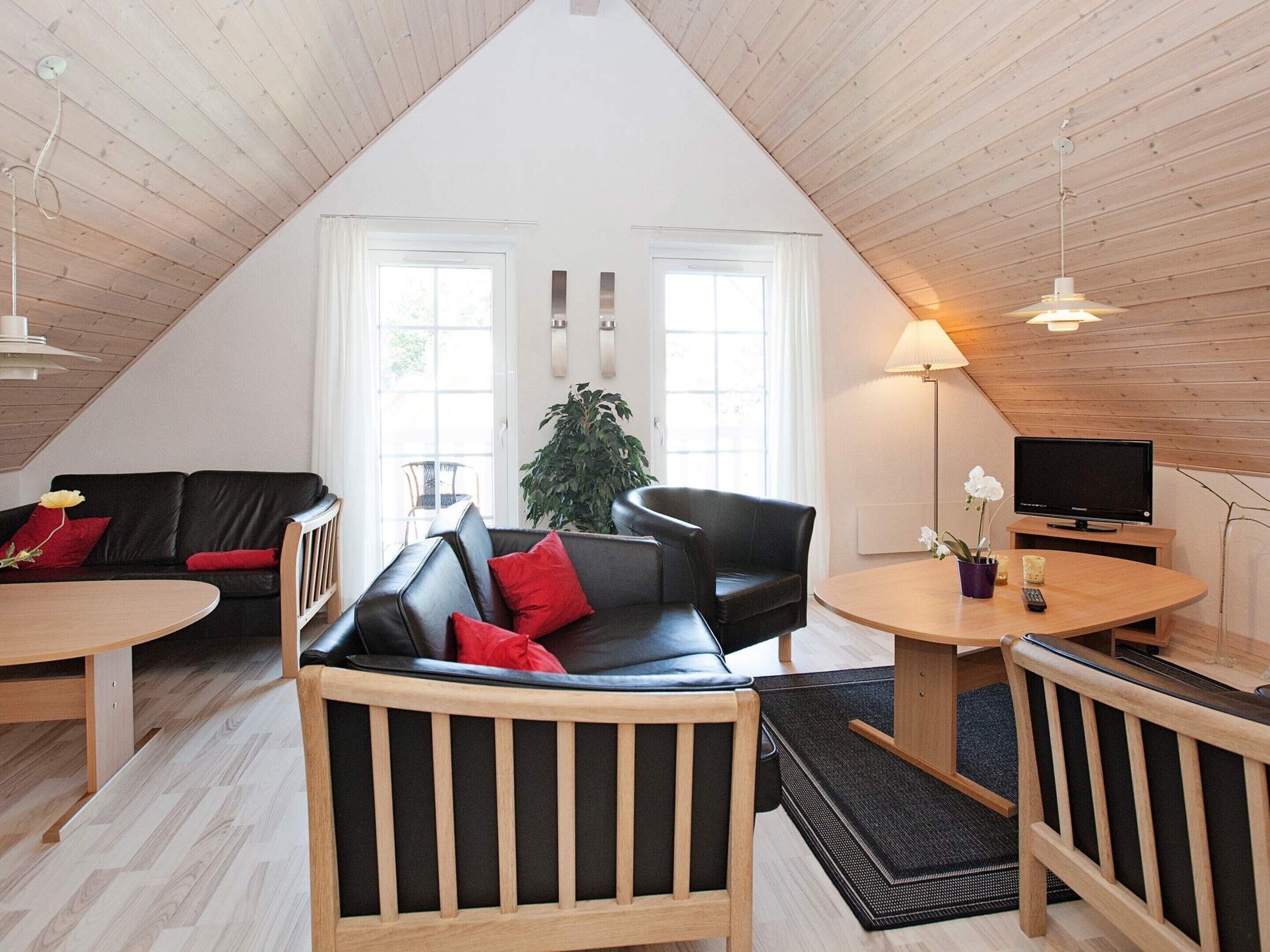 Ein gemütliches Loft-Wohnzimmer mit hohen Decken, einem schwarzen Ledersofa, einem Holztisch und einem Fernseher auf einem Holzständer.