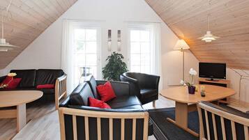 Ein gemütliches Loft-Wohnzimmer mit hohen Decken, einem schwarzen Ledersofa, einem Holztisch und einem Fernseher auf einem Holzständer.