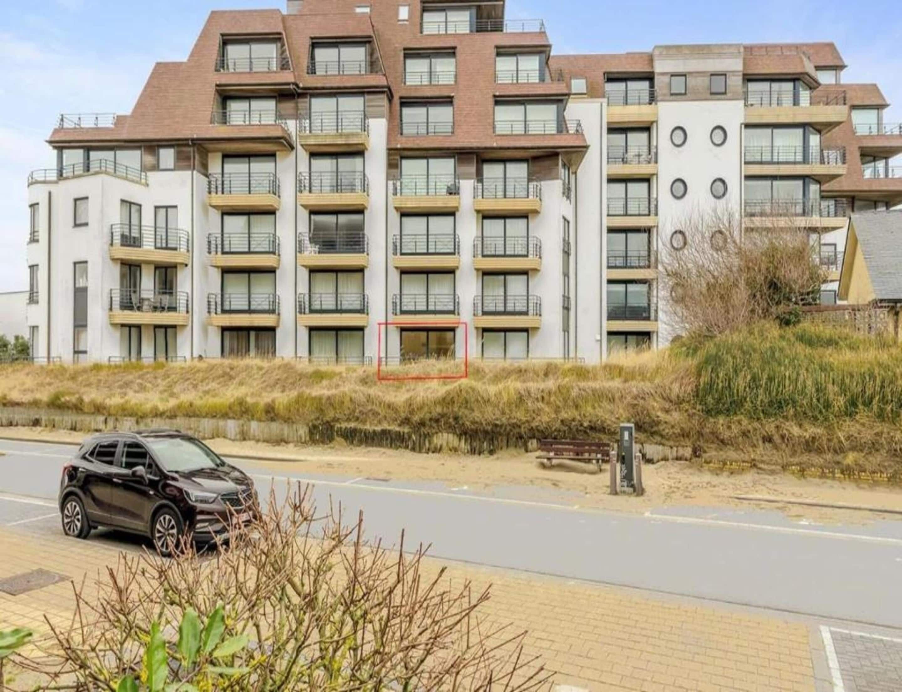 Een modern appartementencomplex met meerdere balkons en een parkeerplaats ervoor.