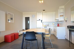 A modern kitchen with white cabinets, a dining table with chairs, and a red bench. - Apartment in Oostduinkerke With Sea View (Koksijde)