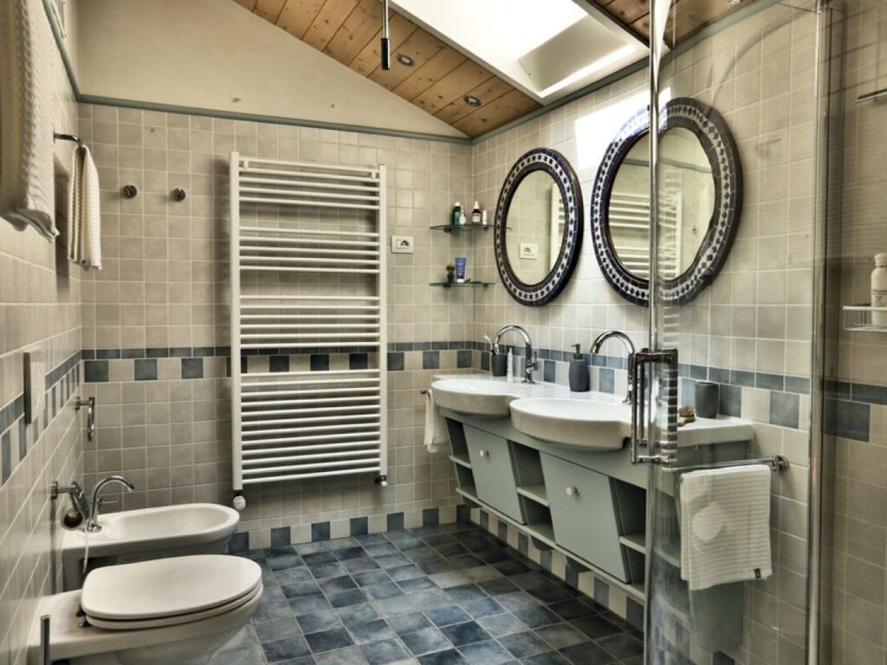 A bathroom with two sinks, a toilet, a towel rack, and a glass shower enclosure.