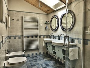 A bathroom with two sinks, a toilet, a towel rack, and a glass shower enclosure.