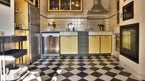 A kitchen with a checkered floor, stainless steel appliances, and yellow cabinets. - Holiday Home Casa Nanda (Mombaruzzo)
