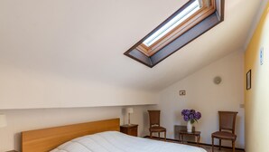 A bedroom with a sloped ceiling, a skylight, a bed, two chairs, a small table, and a vase with flowers. - Holiday Home Les Hirondelle for 8 Persons (Bievre)