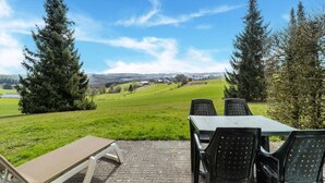 An outdoor seating area with a table and chairs, overlooking a green field and distant buildings. - Holiday Home Les Hirondelle for 8 Persons (Bievre)