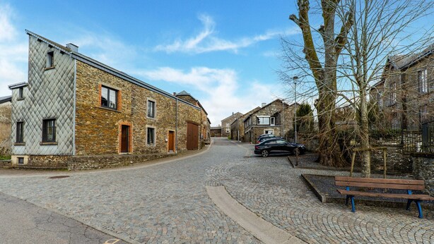 A cobblestone street lined with historic stone buildings, a parked car, and a bench. - Holiday Home Les Hirondelle for 8 Persons (Bievre)