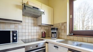 A kitchen with a microwave, oven, dishwasher, coffee maker, and a window with a view of trees. - Holiday Home Les Hirondelle for 8 Persons (Bievre)