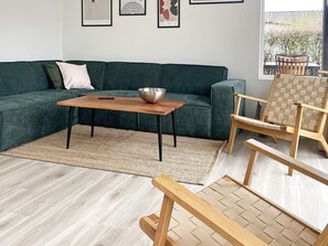 A modern living room with a green sofa, a wooden coffee table, a woven rug, and a wooden chair with a woven seat.