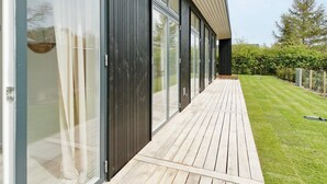 A modern building with large sliding glass doors, a wooden deck, and a well-maintained lawn. - 5 Star Holiday Home in Nysted (Nysted)