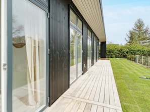 A modern building with large sliding glass doors, a wooden deck, and a well-maintained lawn. - 5 Star Holiday Home in Nysted (Nysted)
