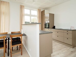 A modern kitchen with a dining area, featuring a built-in oven, a countertop, and wooden chairs.