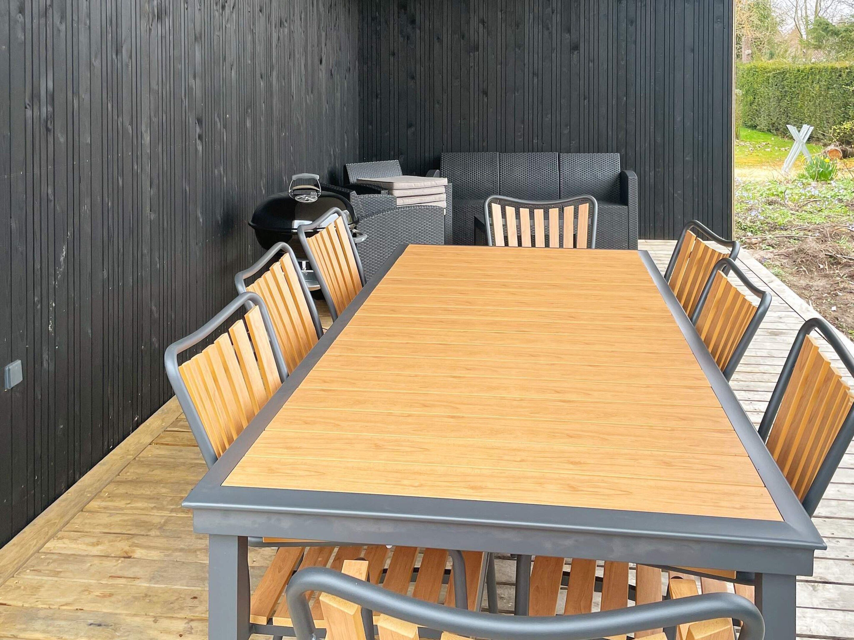 A wooden table with metal chairs, a grill, and a black wall.