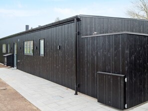 A modern building with a dark exterior, a flat roof, and a paved walkway.