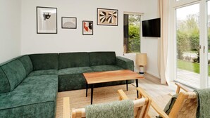 A modern living room with a green sectional sofa, a wooden coffee table, and a TV mounted on the wall. - 5 Star Holiday Home in Nysted (Nysted)