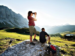 Deux personnes se tiennent sur un promontoire rocheux, d’où elles dominent un paysage montagneux. On aperçoit un lac et une table de pique-nique au loin.