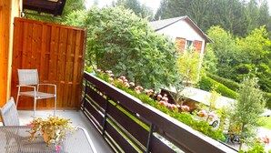 A balcony with a table and chairs, a wooden fence, and a view of a garden and buildings. - Apartment With Sauna and Lakeview (Hermagor-Pressegger See)