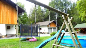 A wooden swing set, a trampoline, and a slide in a backyard with a swimming pool. - Apartment With Sauna and Lakeview (Hermagor-Pressegger See)