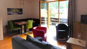 A modern living room with a sofa, chairs, a dining table, and a TV. - Apartment With Sauna and Lakeview (Hermagor-Pressegger See)