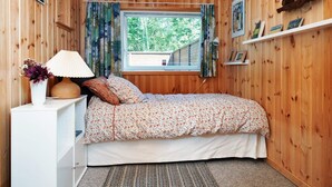 A cozy bedroom with a wooden interior, a bed with floral bedding, a bedside lamp, and a window with curtains. - 5 Person Holiday Home in Frederiksvaerk (Frederiksvaerk)
