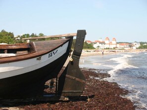 A boat with the name "BINZ" on a beach with waves and buildings in the background.