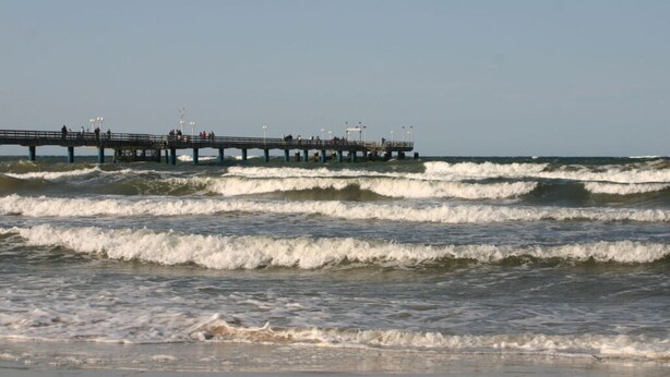Un muelle que se adentra en el océano, con olas rompiendo en la orilla.