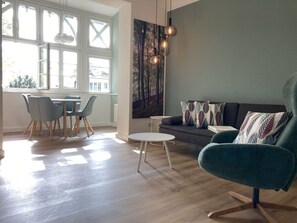 A modern living room with a sofa, chairs, a dining table, and a painting on the wall.