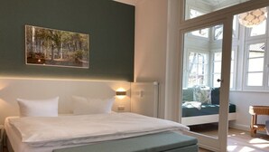 Un dormitorio con cama, banco y vista a una zona de estar exterior a través de una puerta de vidrio.