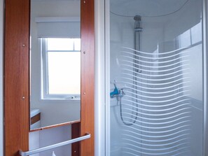 Ein Badezimmer mit Holztür, Fenster und Duschkabine mit Glastür.