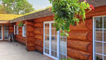 Une cabane en rondins dotée d’une terrasse en bois, de grandes fenêtres et de jardinières suspendues.