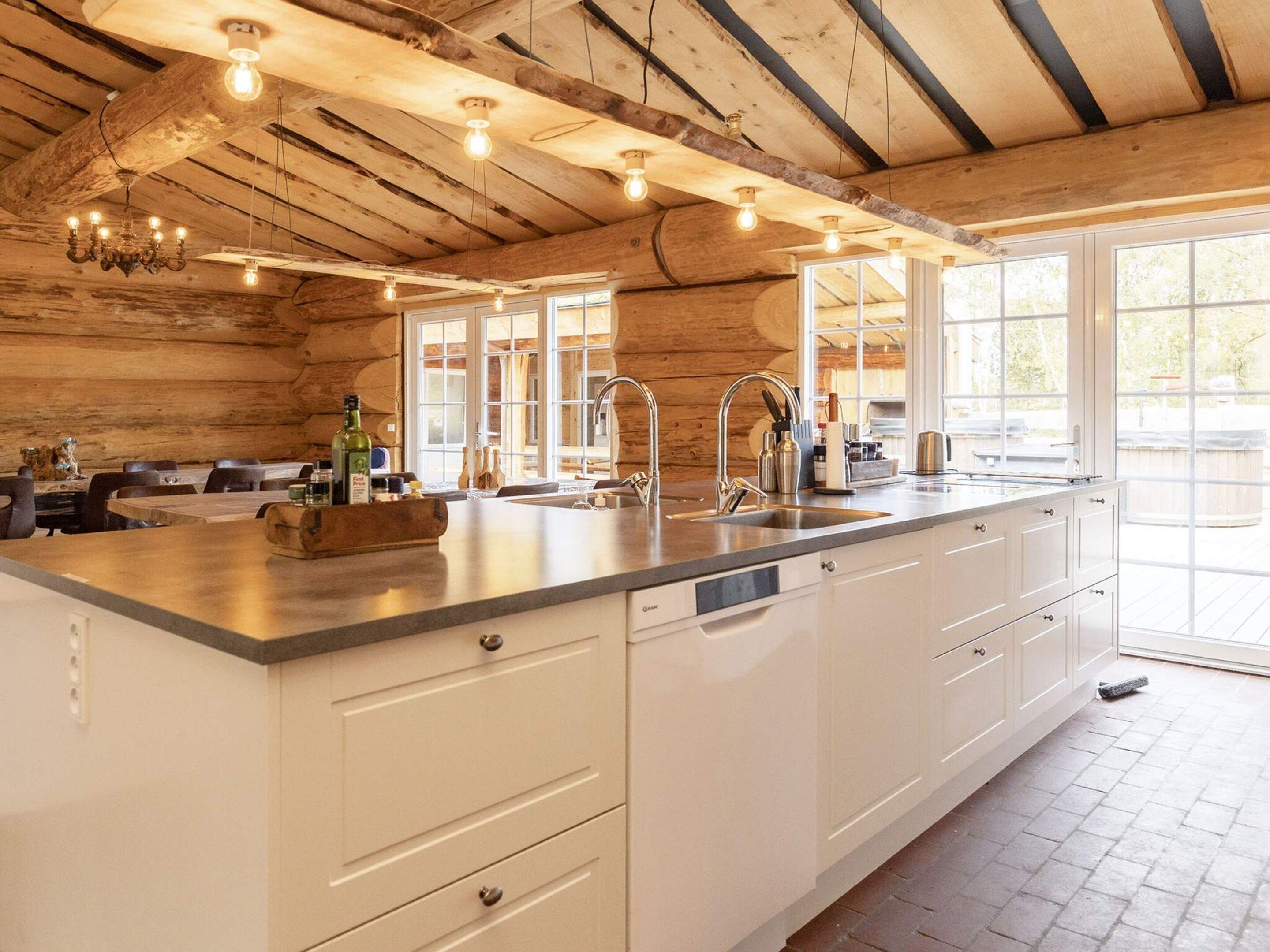 A kitchen with a large island, white cabinetry, a farmhouse-style ceiling with exposed beams, and a large window providing natural light.