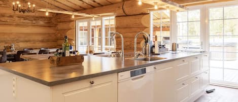 A kitchen with a large island, white cabinetry, a farmhouse-style ceiling with exposed beams, and a large window providing natural light.