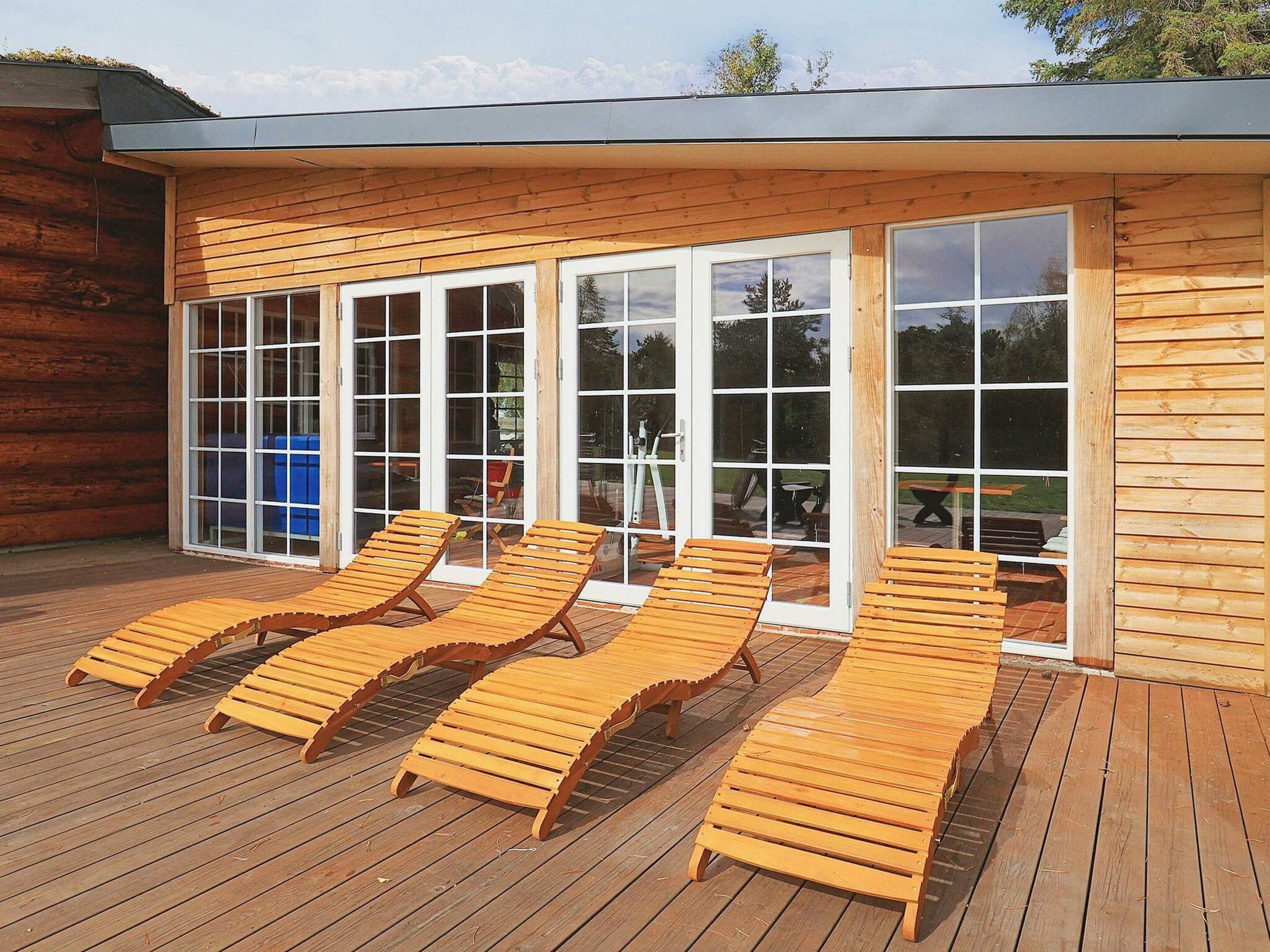 A wooden deck with sun loungers and a glass door leading to an outdoor area.