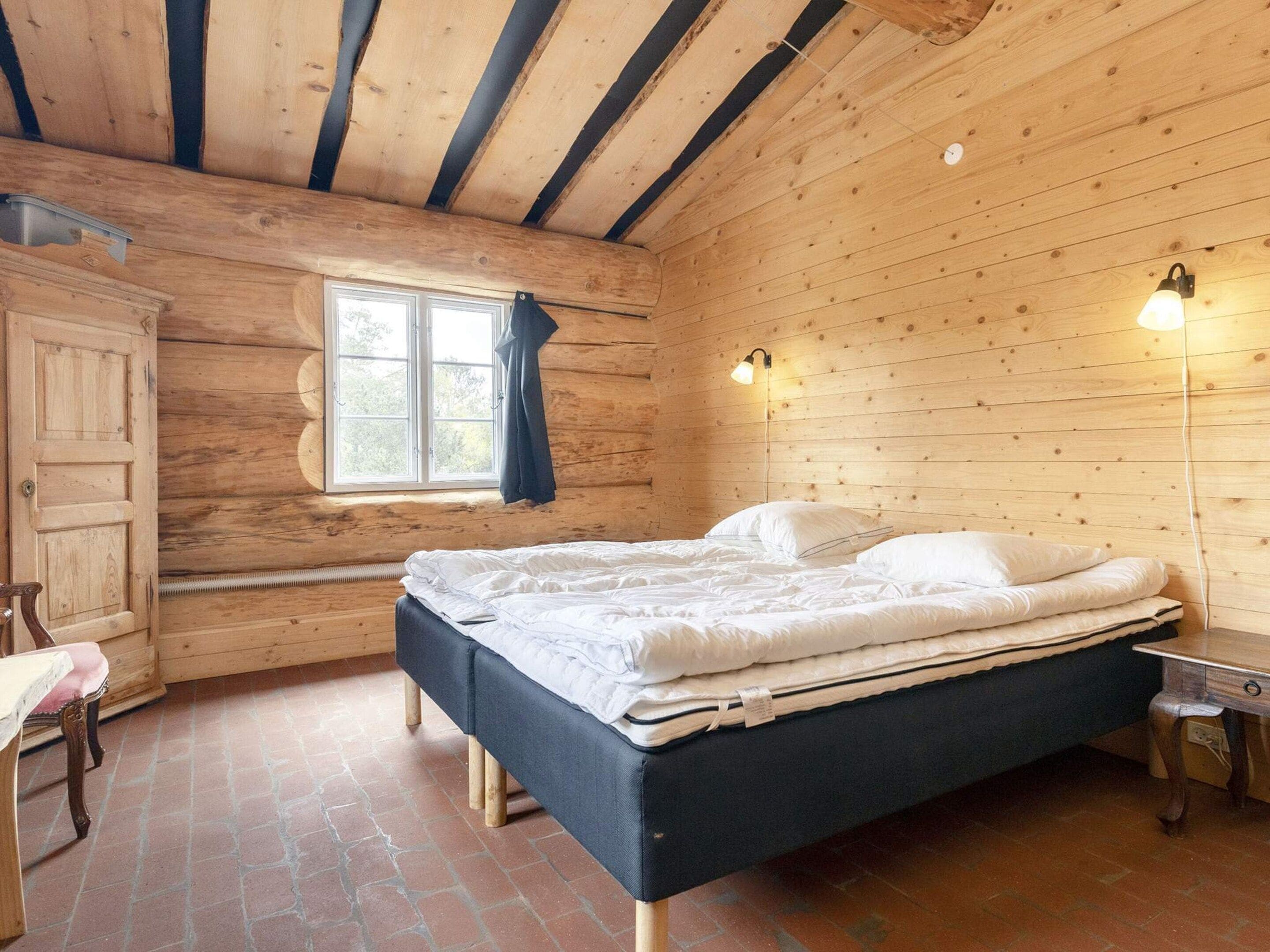 Una habitación de madera con una cama, un ventanal y una mesita de noche.