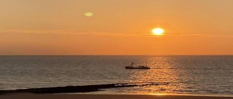 Un atardecer sobre un mar tranquilo con un barco a lo lejos.