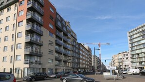A multi-story residential building with balconies, a pedestrian crossing, and a construction crane in the background. - Sleek Stay by the Sea (Middelkerke)