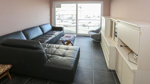 A living room with a black leather sofa, a small wooden table, and a white cabinet. - Sleek Stay by the Sea (Middelkerke)