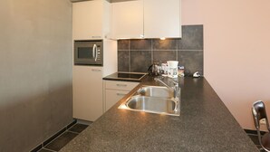 A compact kitchen with a built-in microwave, a coffee maker, and a stainless steel sink. - Sleek Stay by the Sea (Middelkerke)