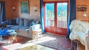 A cozy room with a wooden ceiling, a sofa, a chair, a table, and a large window with curtains. - 8 Person Holiday Home in Tjorhom (Sirdal)