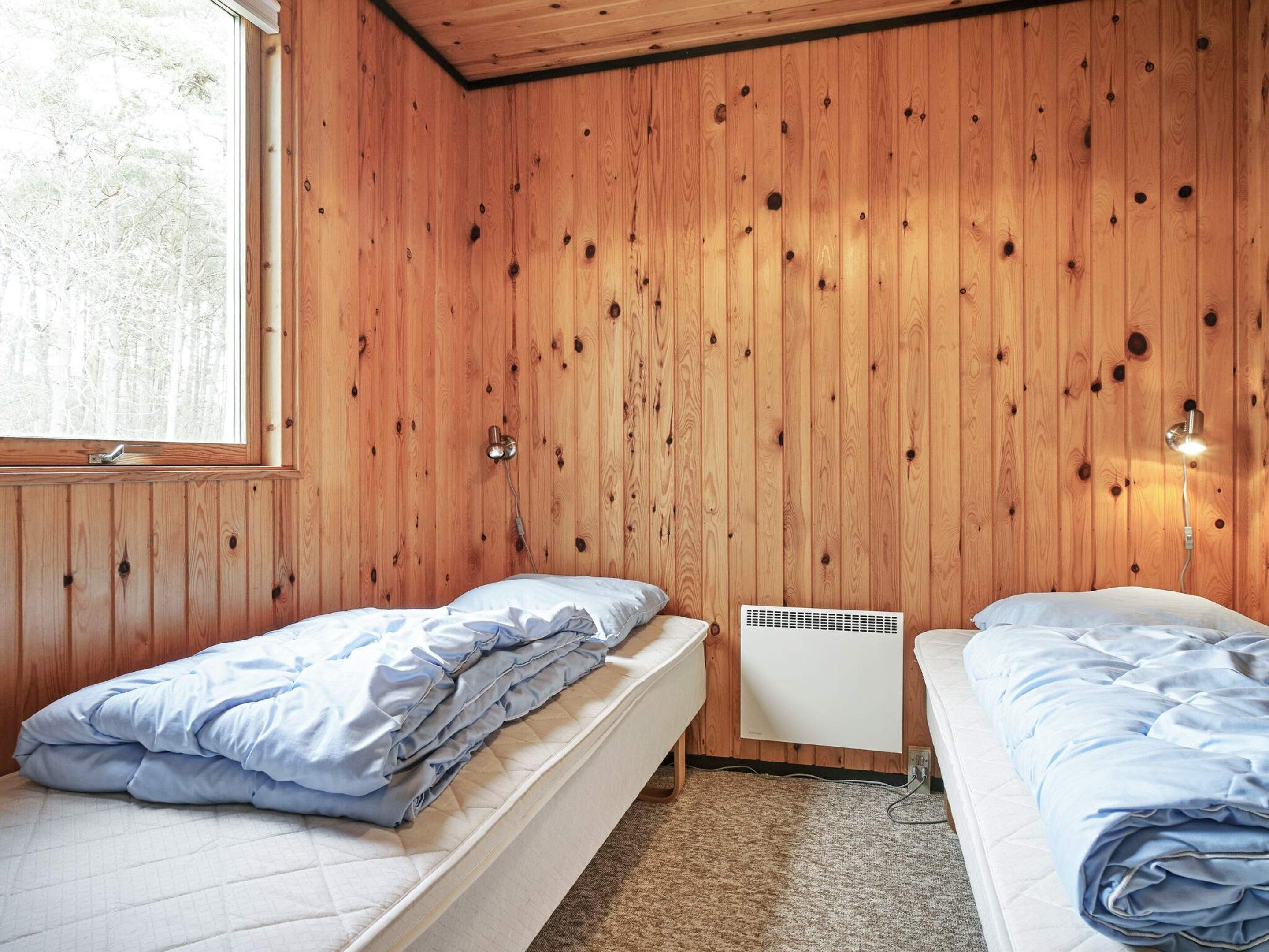 A room with two beds, wooden walls, a window, and a wall-mounted heater.