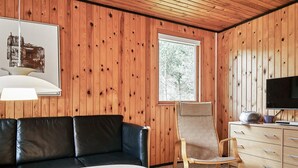 A room with a wooden paneled wall, a black leather sofa, a wooden chair, a marble table, and a television on a wooden cabinet. - 6 Person Holiday Home in Aakirkeby (Akirkeby)