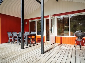 An outdoor deck with a wooden floor, a table with chairs, and a barbecue grill.