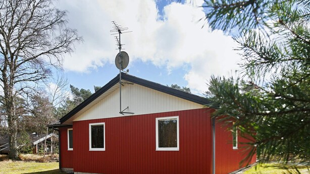 A red building with a satellite dish, two windows, and a small porch. - 6 Person Holiday Home in Aakirkeby (Akirkeby)