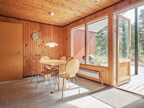 Interior em madeira com mesa e cadeiras, luminária pendente e janela com vista para o exterior.